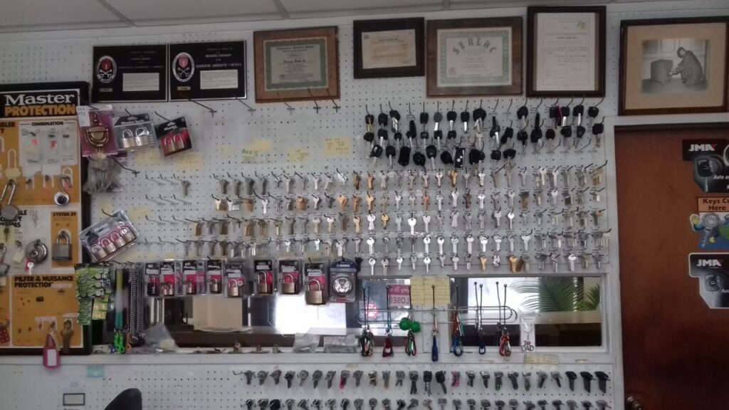 The wall behind the counter at Rudd Lockmasters, lined with hundreds of house, car and padlock key blanks, with framed certificates and an old photograph above.